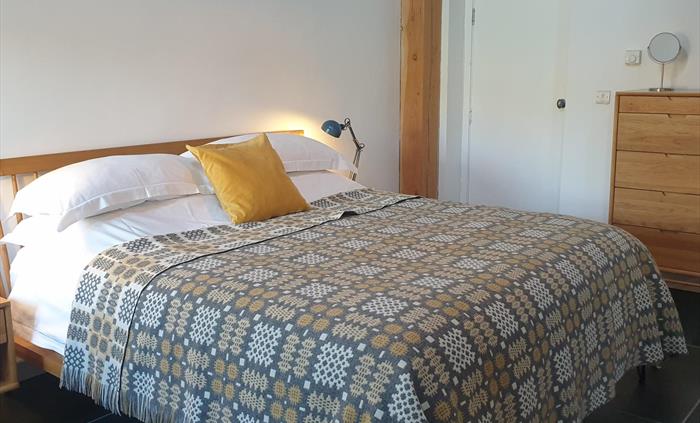 Oak superking bed made up with crisp white linen and a contemporary Welsh blanket in pale grey and yellow.